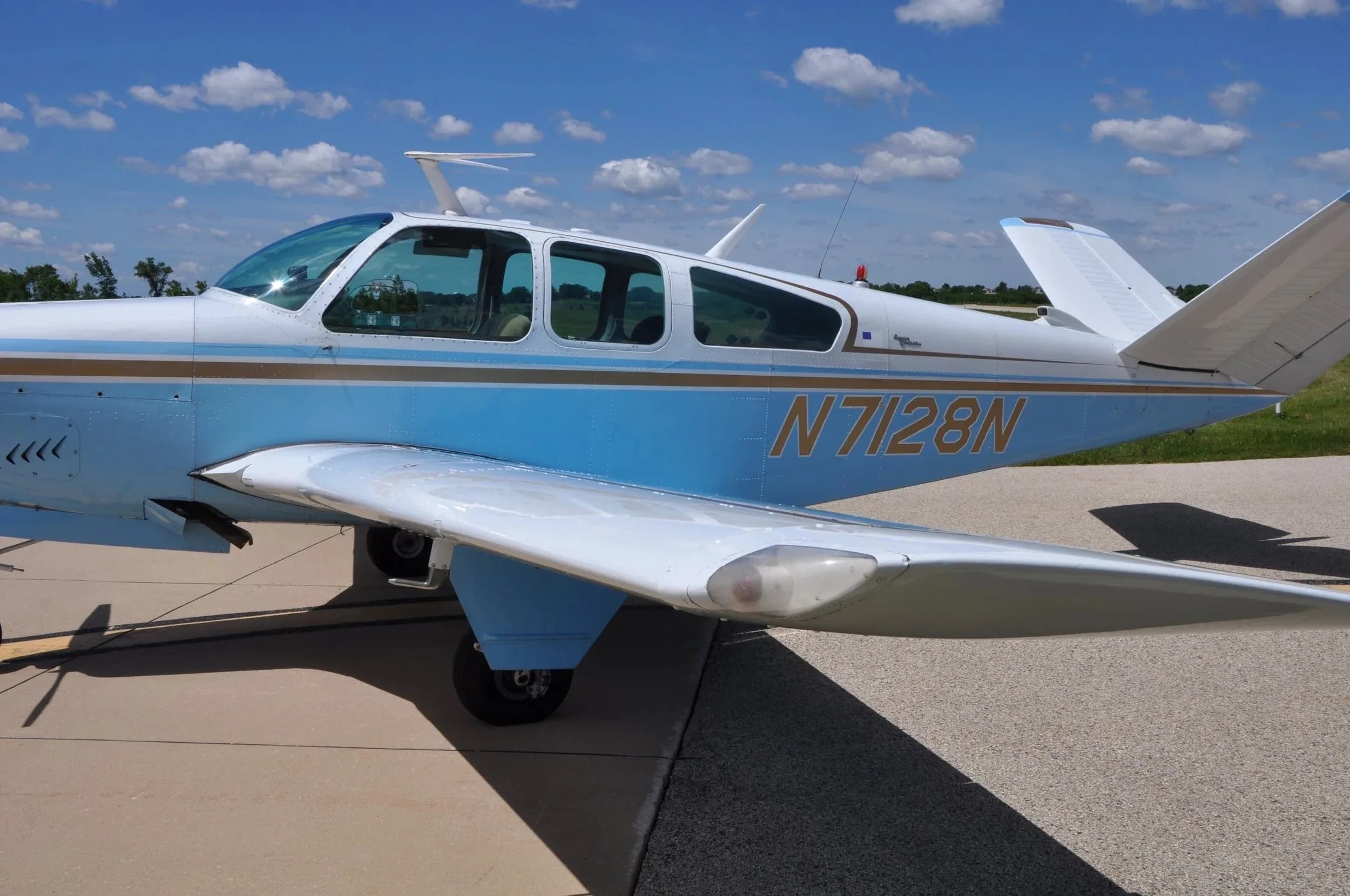 A close-up side view of the fuselage and wing of the light blue and white Beechcraft Bonanza N7128N.