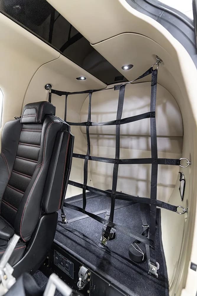 The rear cargo area of the TBM 930 cabin, featuring a black cargo net and a single black leather seat.