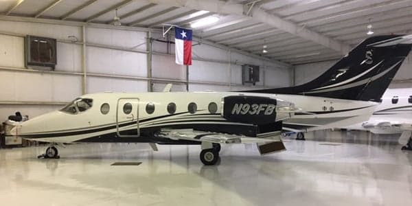A white and black Hawker jet is parked inside a hangar with a Texas flag.