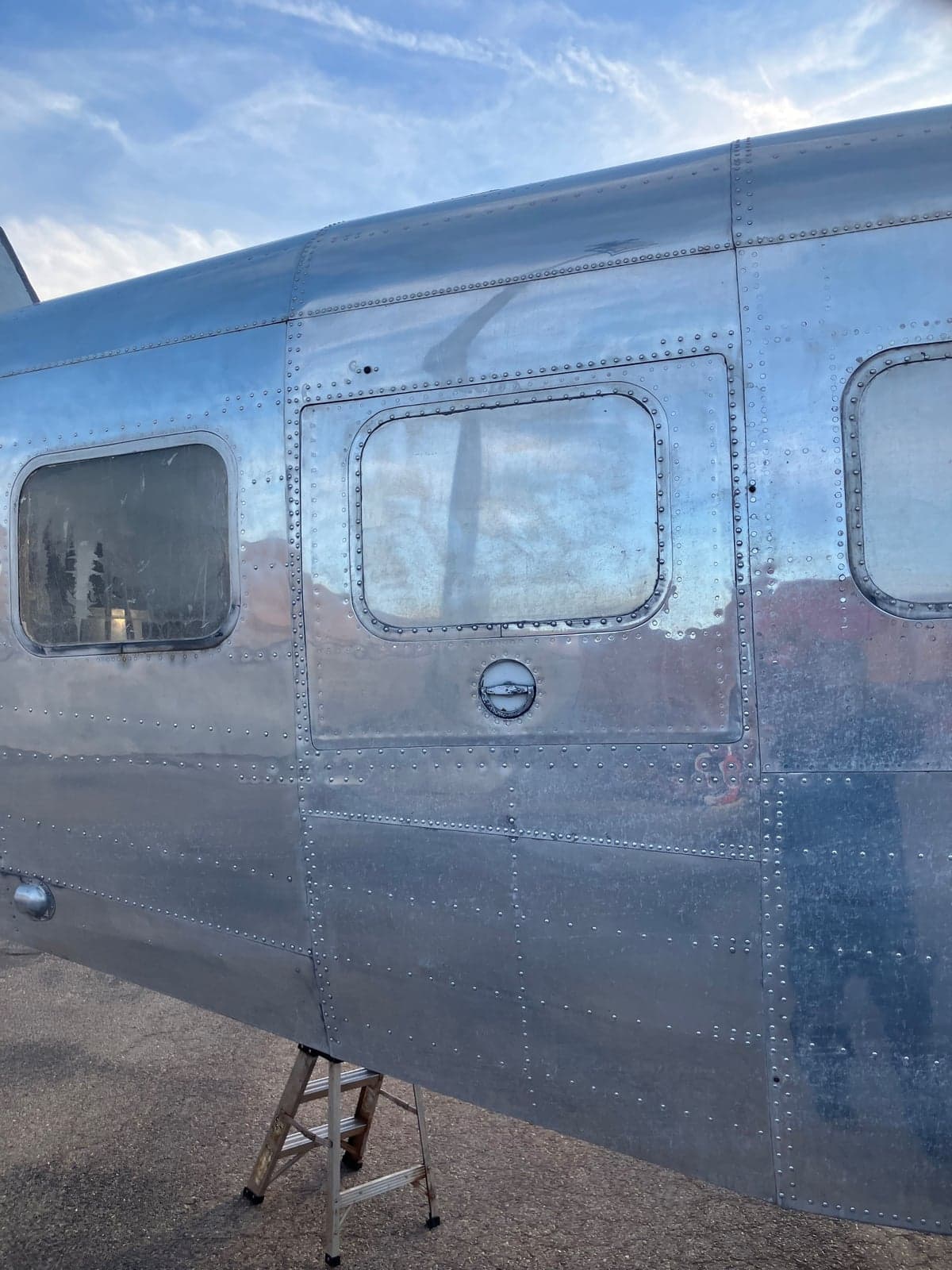 Close-up of the fuselage of a silver Twin Bonanza aircraft, showing the windows and rivets.