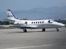 A Cessna Citation CJ1+ aircraft parked on a wet tarmac with a cloudy sky.