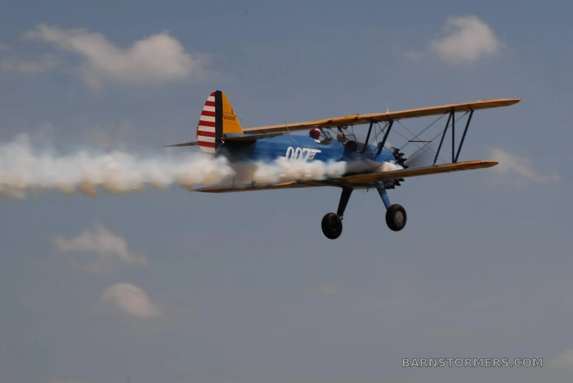 A blue and yellow biplane with "007" on its side flies through the sky, trailing white smoke.