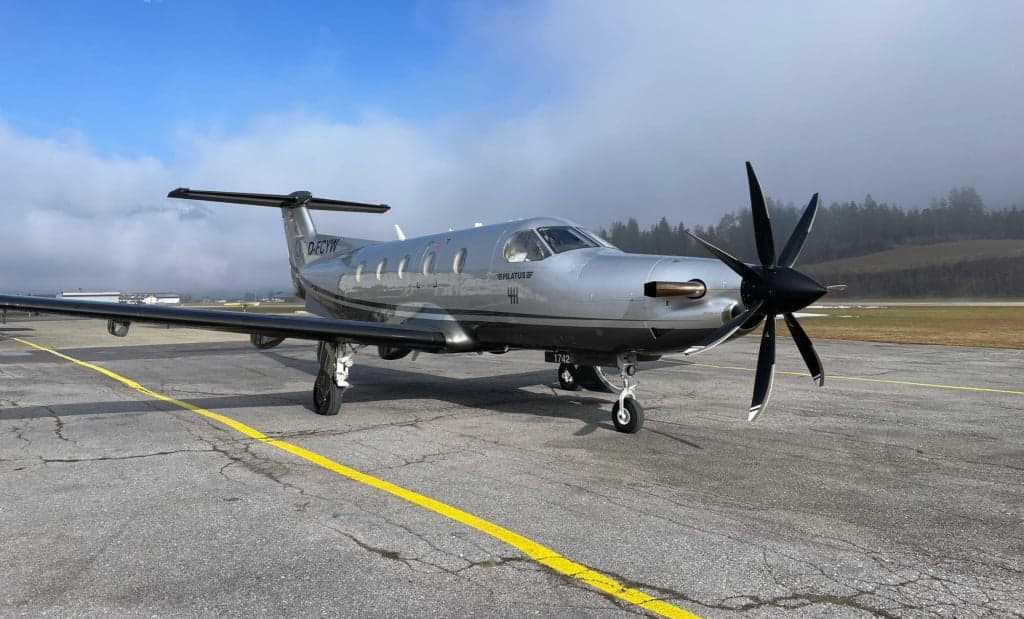Pilatus PC-12 aircraft D-FCYW on the tarmac with a silver and black paint scheme.
