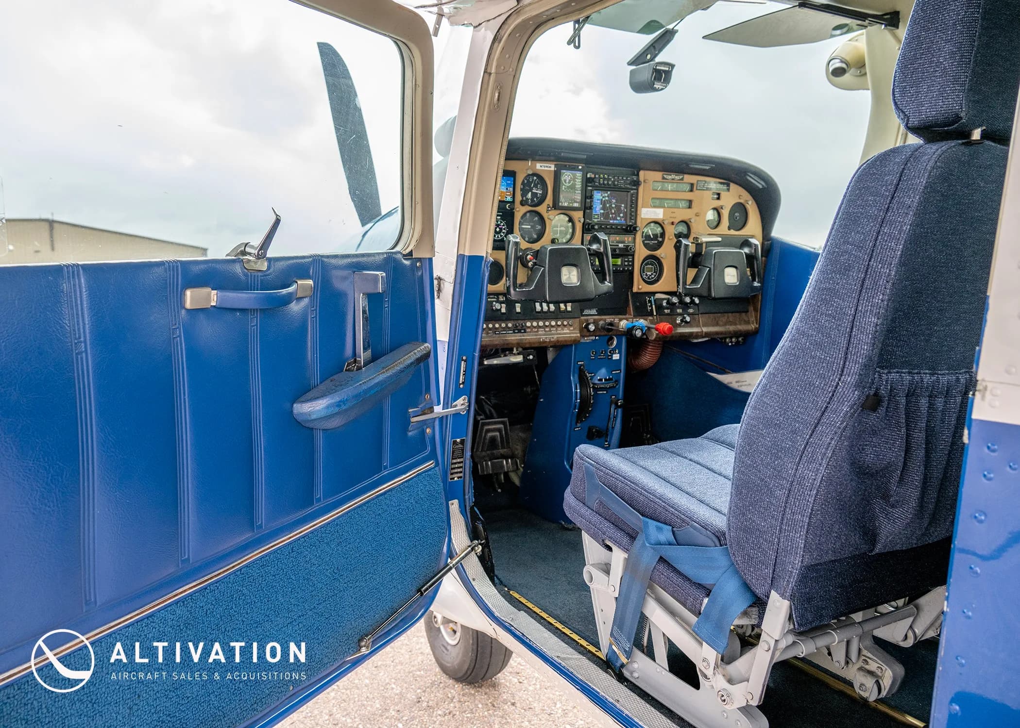 The open door and front blue seat of a Cessna 182, with a partial view of the cockpit instruments.