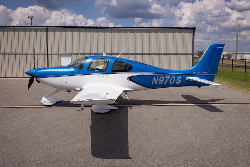 A side view of the blue and white Cirrus SR22 aircraft, N970S, parked on an asphalt ramp next to a hangar.
