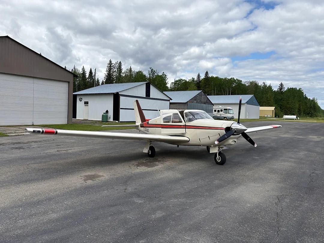 A white and brown aircraft with the registration C-GSUD parked on an airport tarmac with hangars in the background.