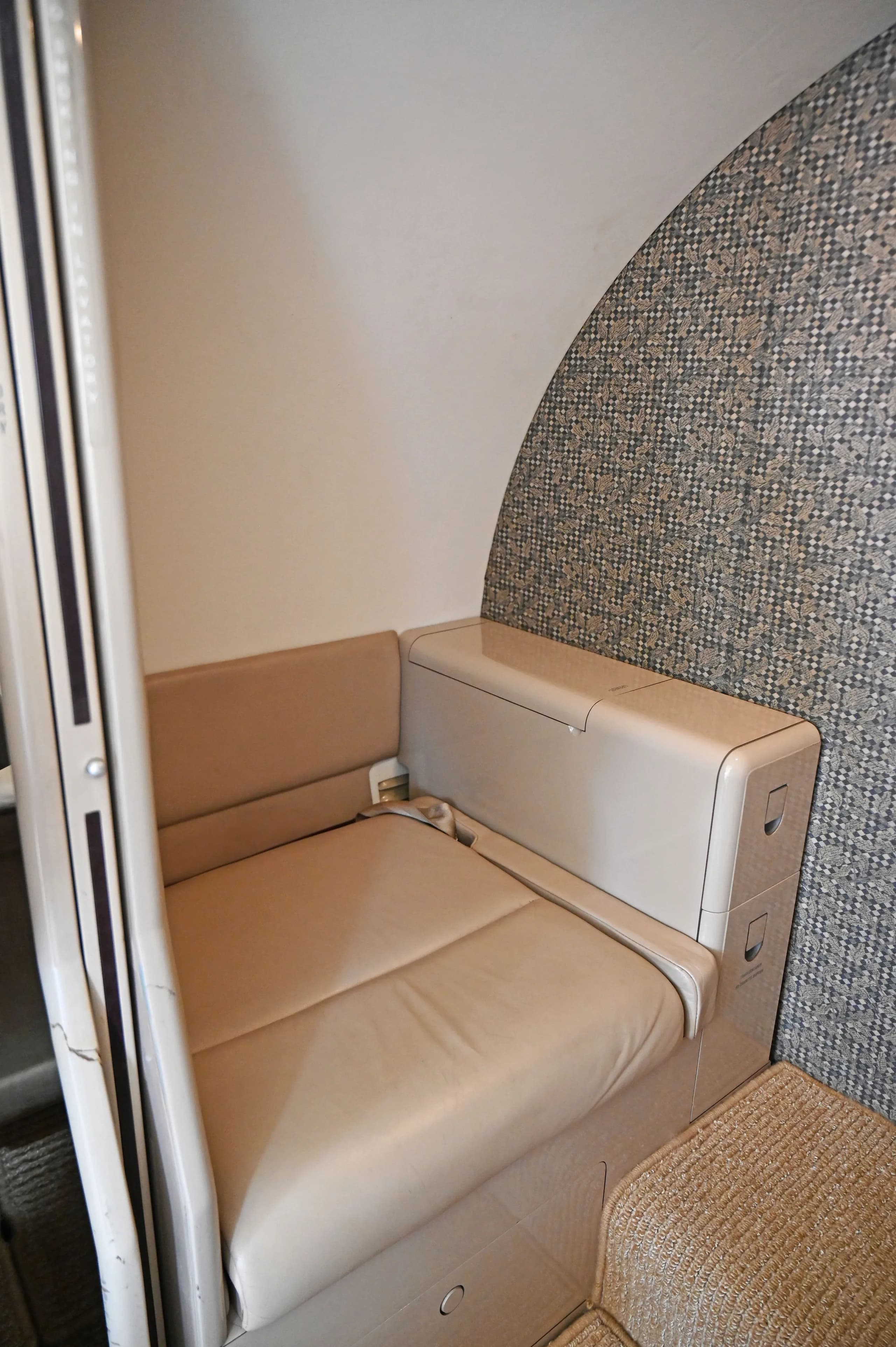 A close-up of a single beige leather bench seat inside a private jet cabin with patterned wall covering.