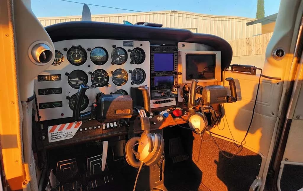 The cockpit instrument panel of the aircraft, featuring analog gauges and modern digital displays, illuminated by golden hour sunlight.