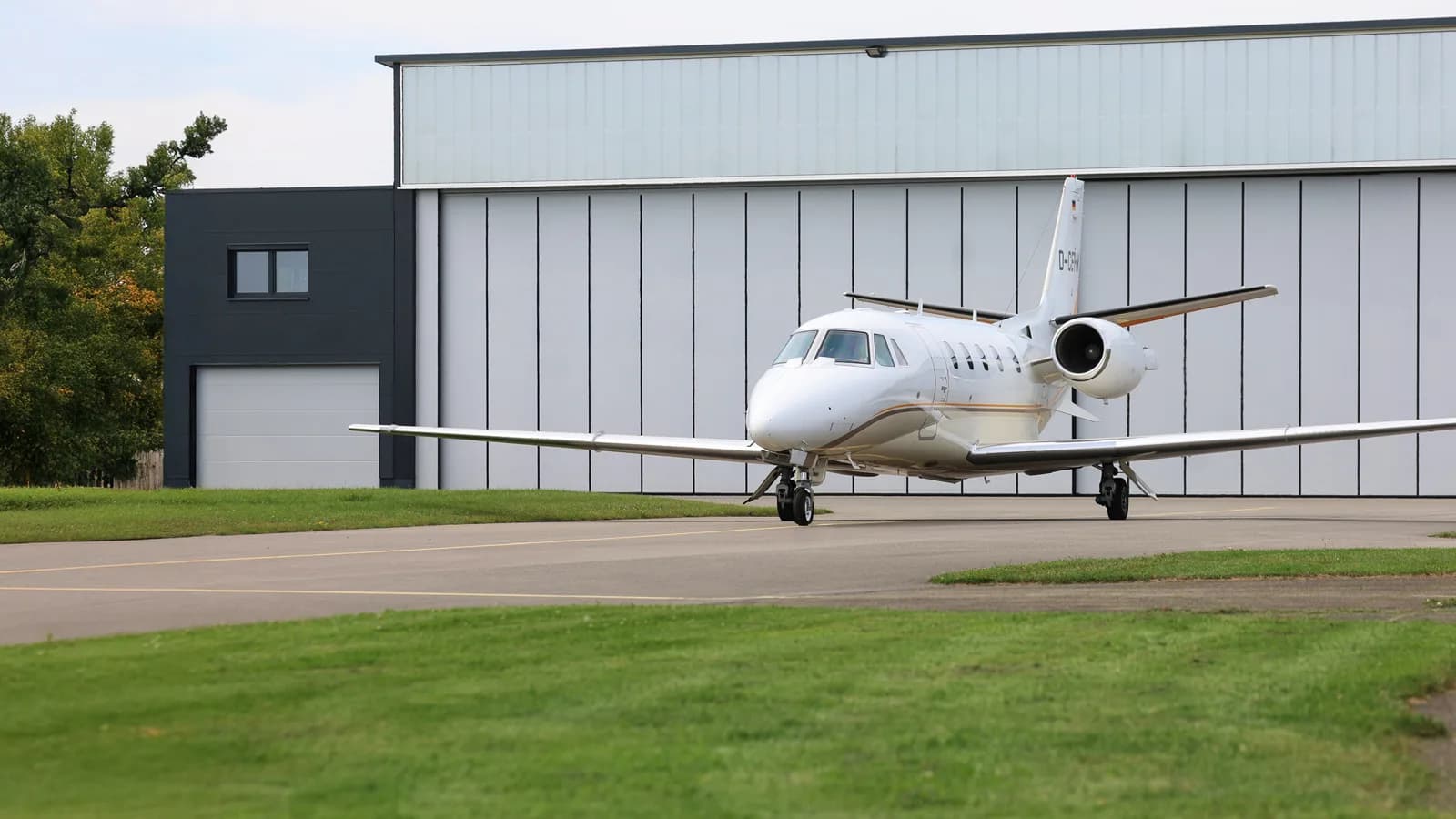 A white Cessna Citation private jet with registration D-CEHM is parked on a tarmac in front of a large hangar.