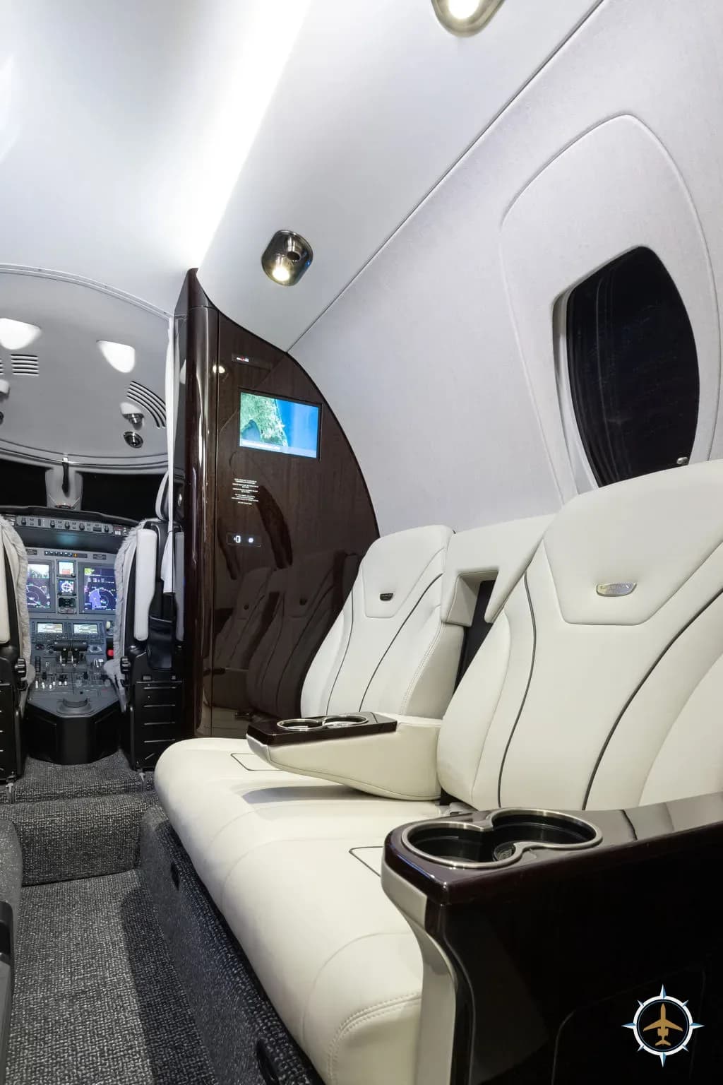The aircraft cabin interior with white leather seats and a view into the cockpit.