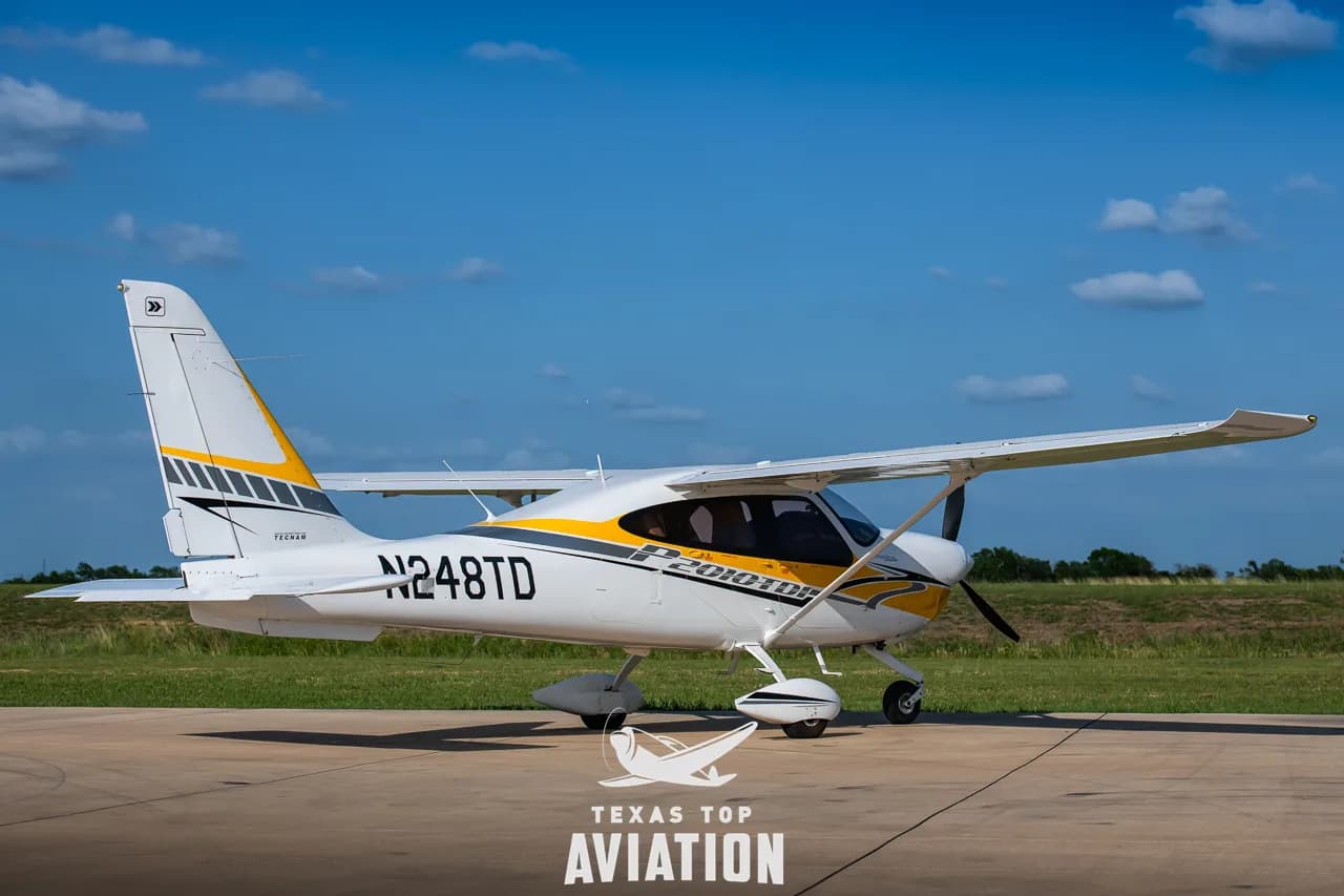 A white and yellow Tecnam P2010 TDI aircraft (N248TD) parked on an airfield under a blue sky.