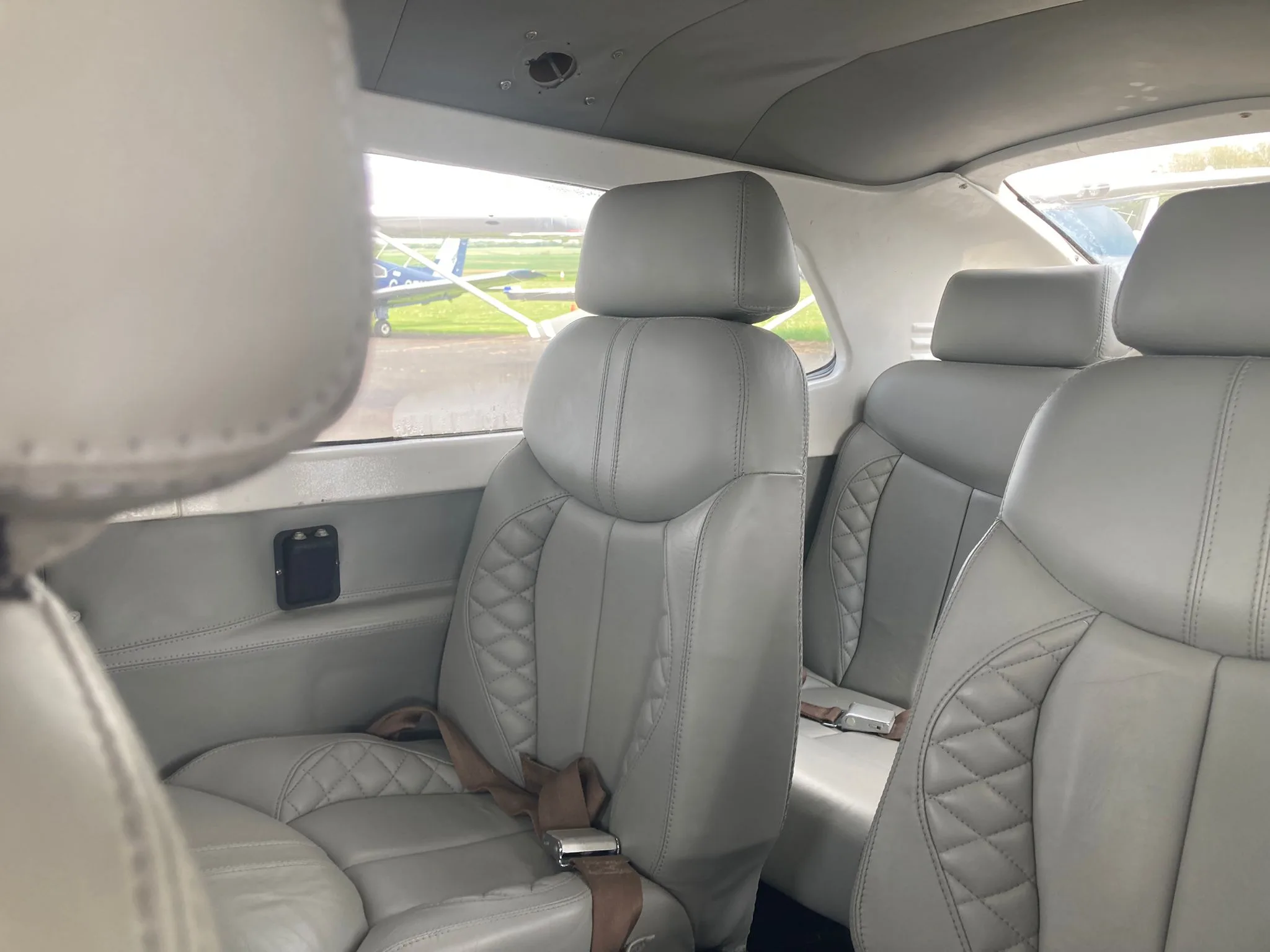 The rear passenger seats of an aircraft, upholstered in light grey leather with quilted stitching, seen from the front.