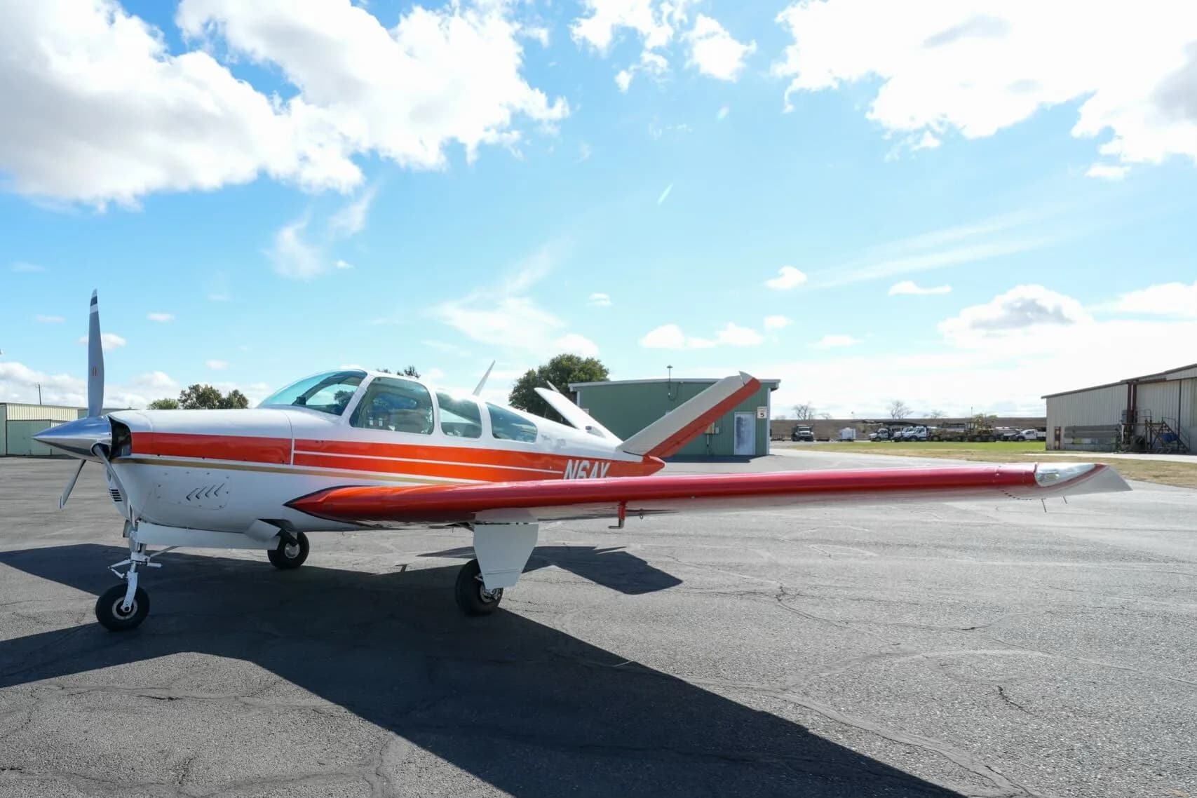 A low-angle view of the white and orange Beechcraft Bonanza N6AY with its wings extended on the tarmac.