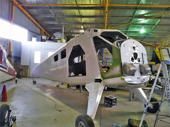 The white fuselage of an aircraft, partially assembled, in a hangar.