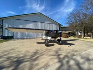 A Carbon Cub aircraft is parked on a concrete pad in front of a building.
