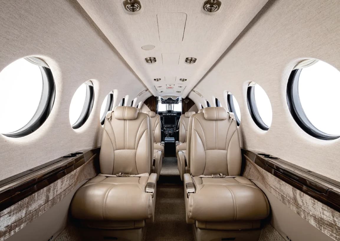 View down the cabin aisle of a King Air 360, showing tan leather seats and light-colored walls.
