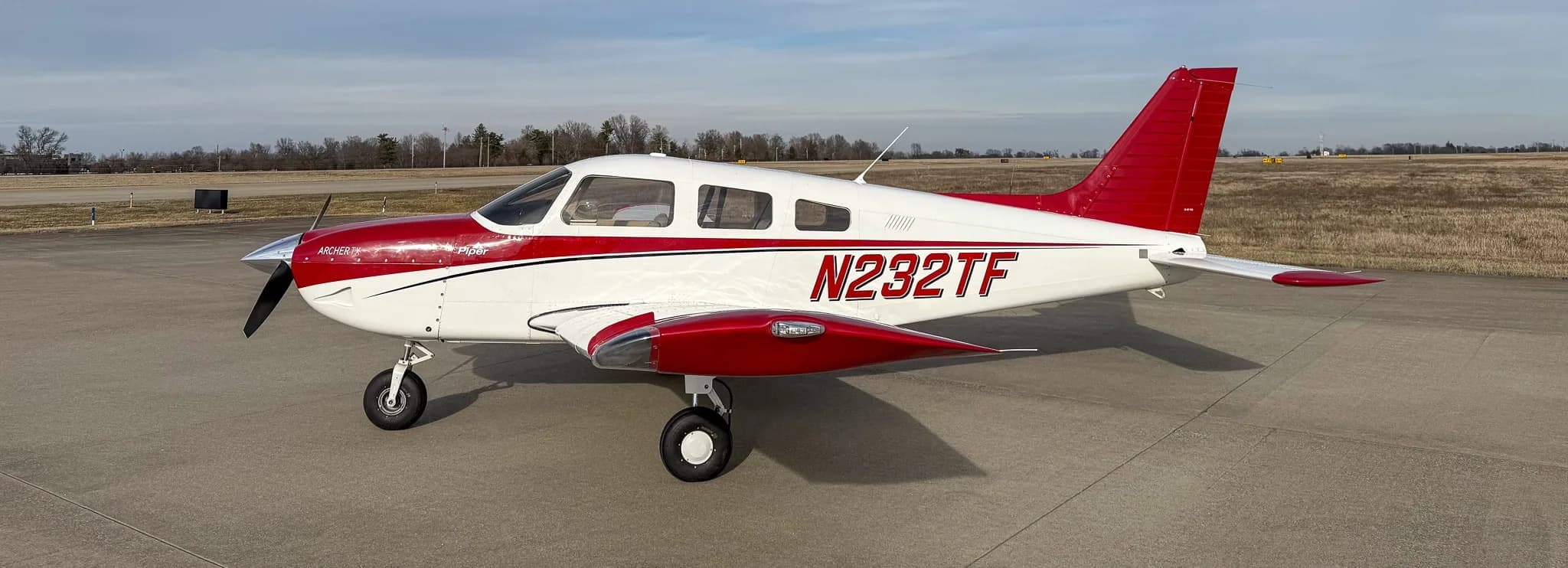 A three-quarter front-right view of a white and red Piper Archer TX, N232TF, parked on an airfield.