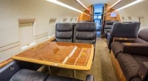Interior of the Challenger aircraft cabin with leather seats and a wooden table.