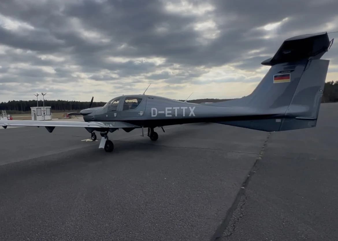 A gray Diamond DA50 RG aircraft is parked on the tarmac under a cloudy sky.