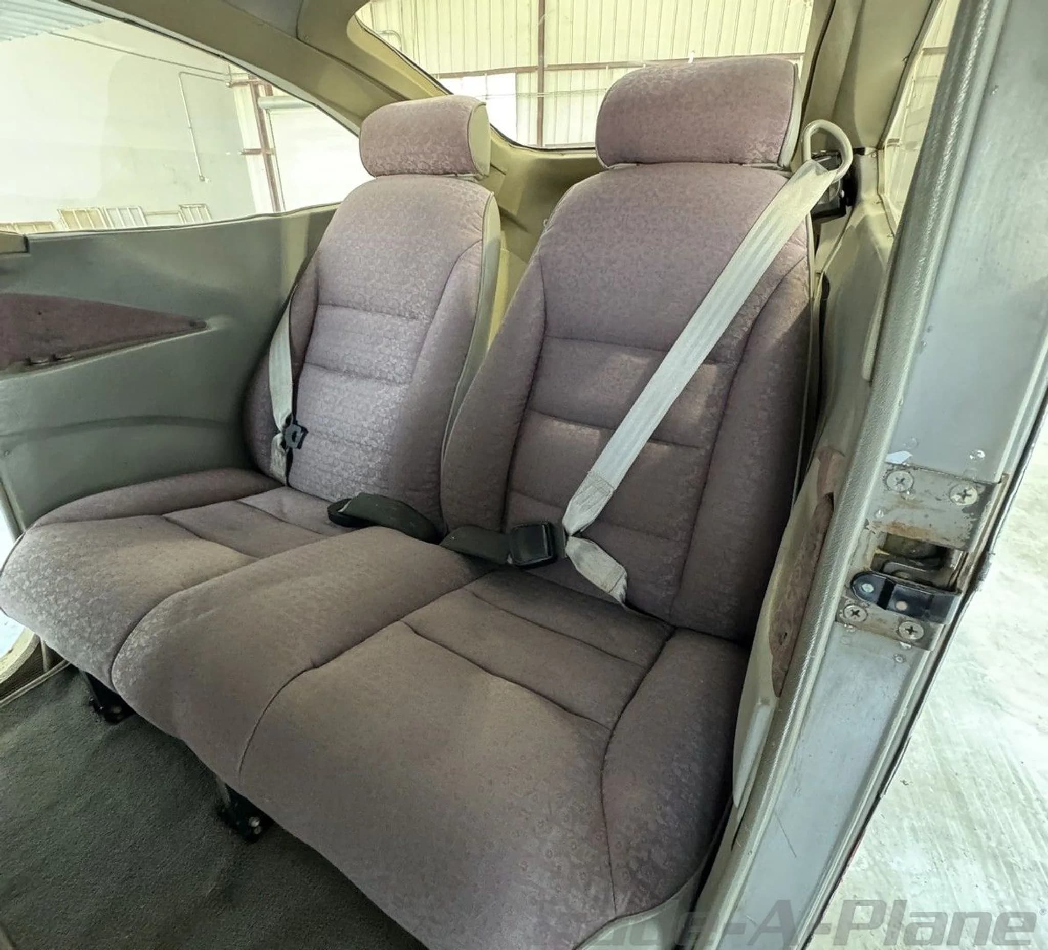 The two rear passenger seats of the aircraft, upholstered in a patterned grey fabric with seatbelts.
