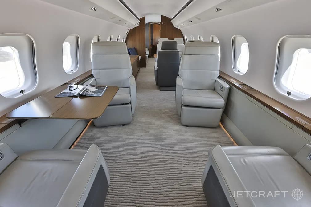 The luxurious cabin interior of a Bombardier Global 6000, featuring light grey leather seats and a wooden table.