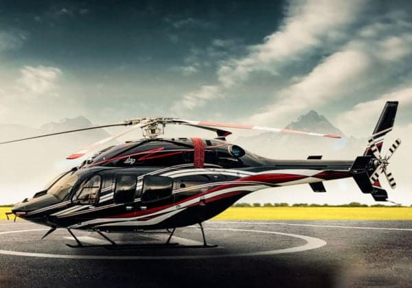A black and white helicopter with red accents sits on a helipad with mountains in the background.