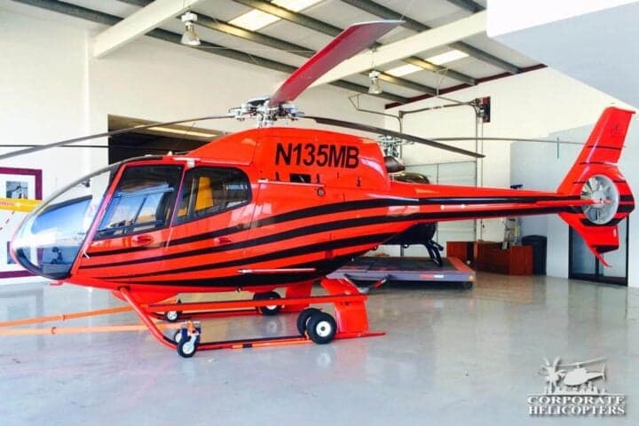 A red and black helicopter with the tail number N135MB inside a hangar.