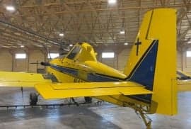 Rear side view of a yellow and blue agricultural aircraft in a hangar.