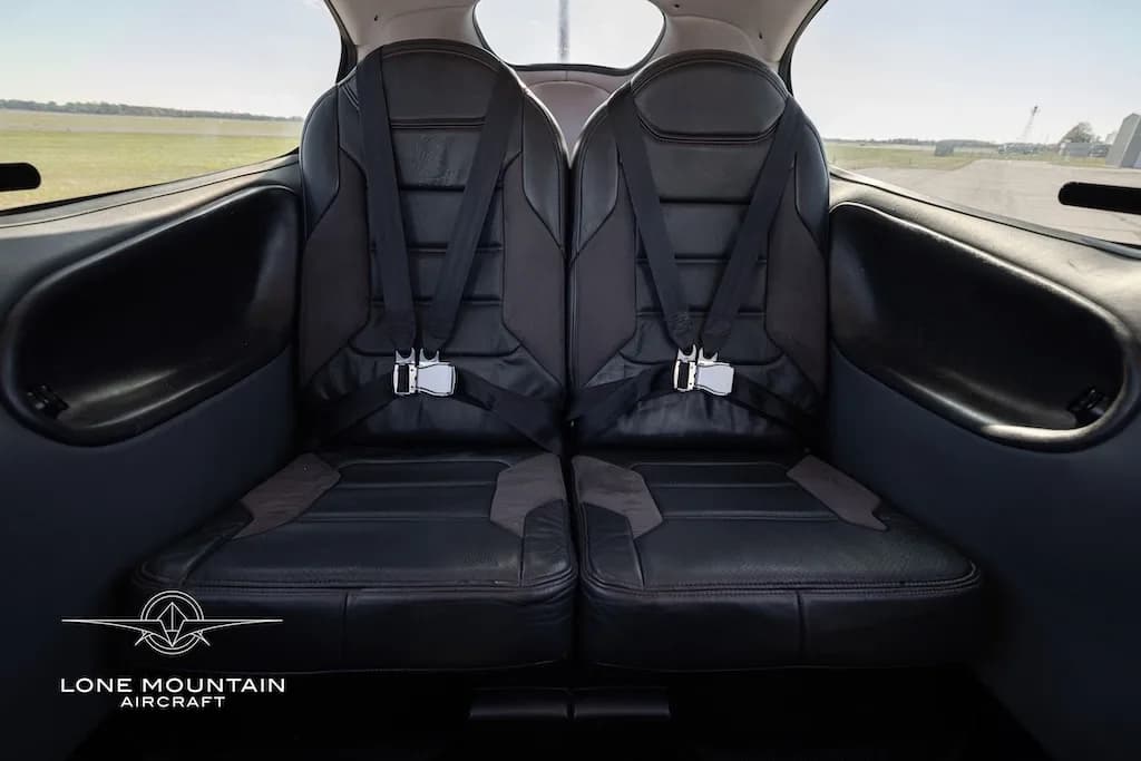 The black leather rear passenger seats of an aircraft cabin with seatbelts fastened.