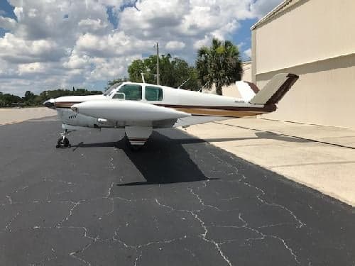 A Beechcraft Bonanza sits on the tarmac in front of a building.