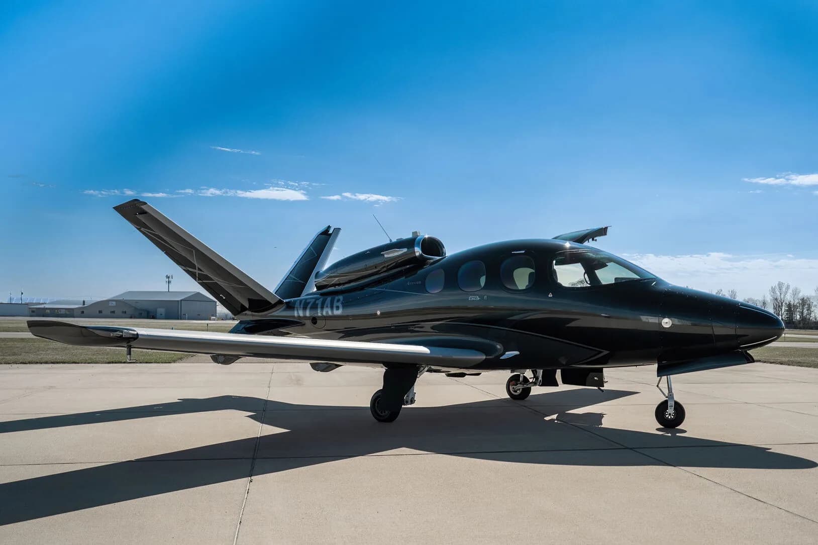 Side view of a black Cirrus Vision Jet (N71AB) with a grey underside and geometric tail design, parked on an airport tarmac.