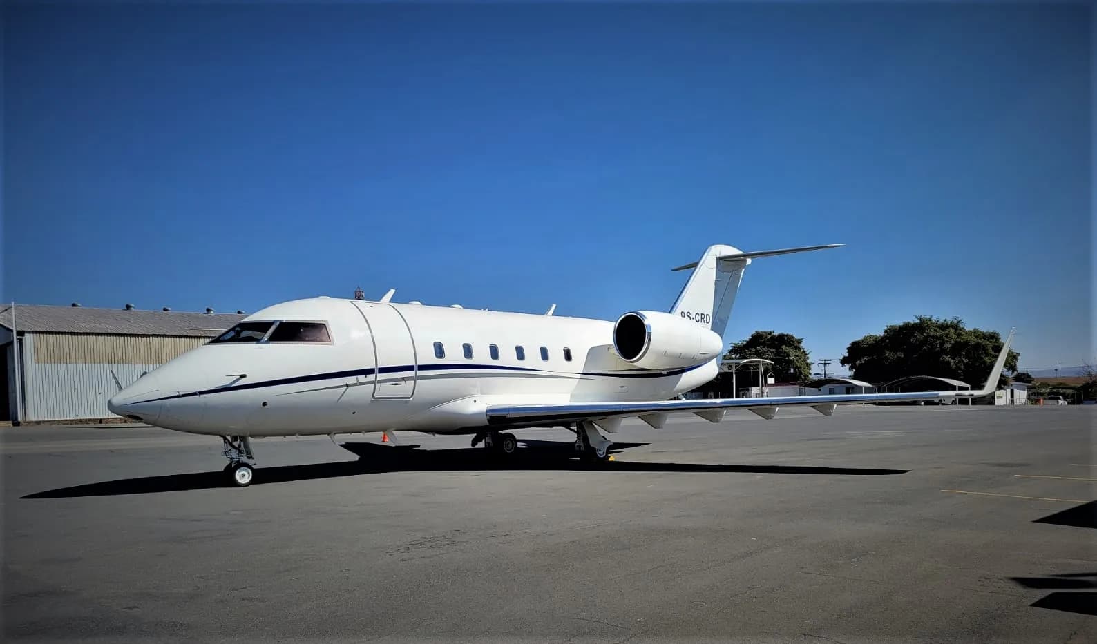 A white Bombardier Challenger business jet parked on an airfield next to a hangar.