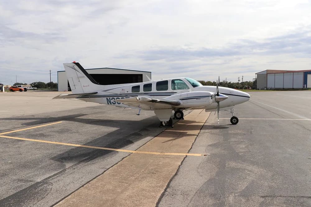 A white and black Beechcraft Baron 58 (N36TC) parked on an asphalt ramp with hangars in the background.