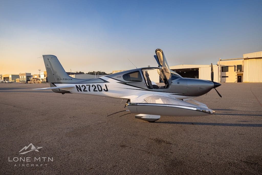 A Cirrus SR22T aircraft with open doors is parked on the tarmac in front of a hangar.