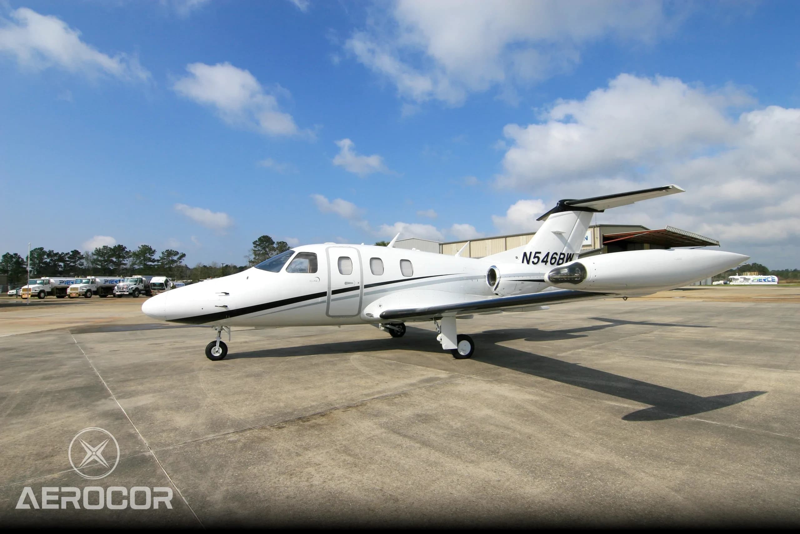A white Eclipse 500 jet with black and grey stripes parked on an airfield, viewed from the front-right.