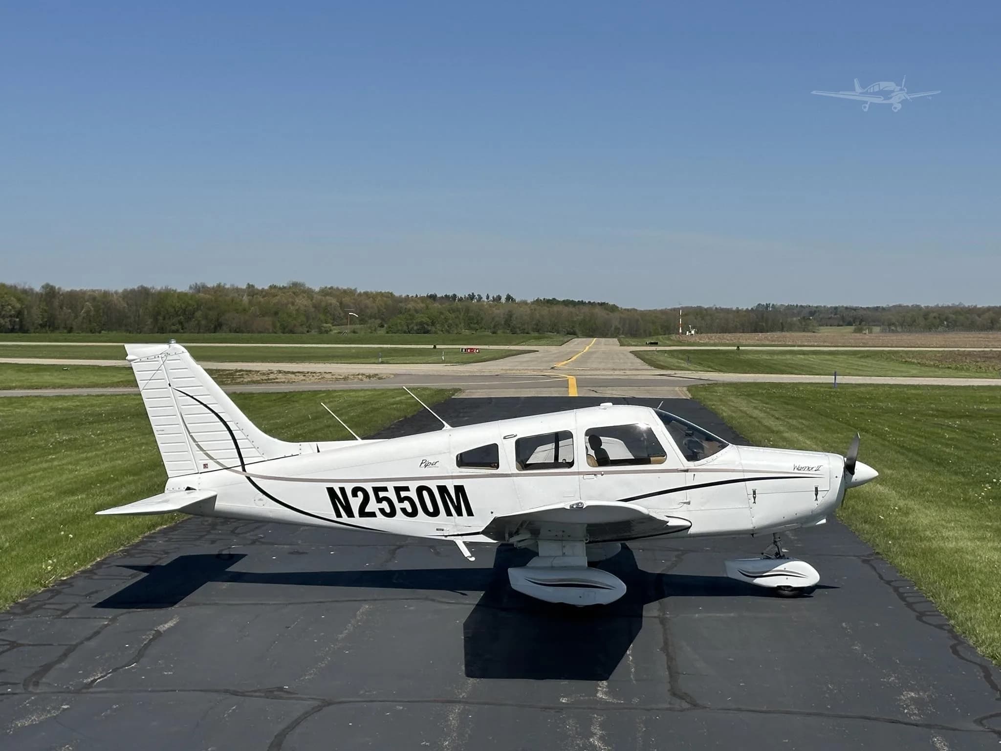 A side view of the white Piper Cherokee aircraft, N2550M, with black accent stripes, parked on a runway.