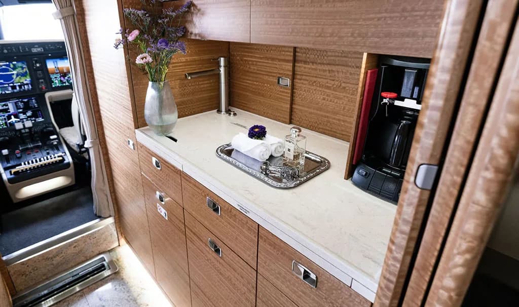 The galley area of a business jet with wooden cabinetry, a countertop, and the cockpit visible in the background.