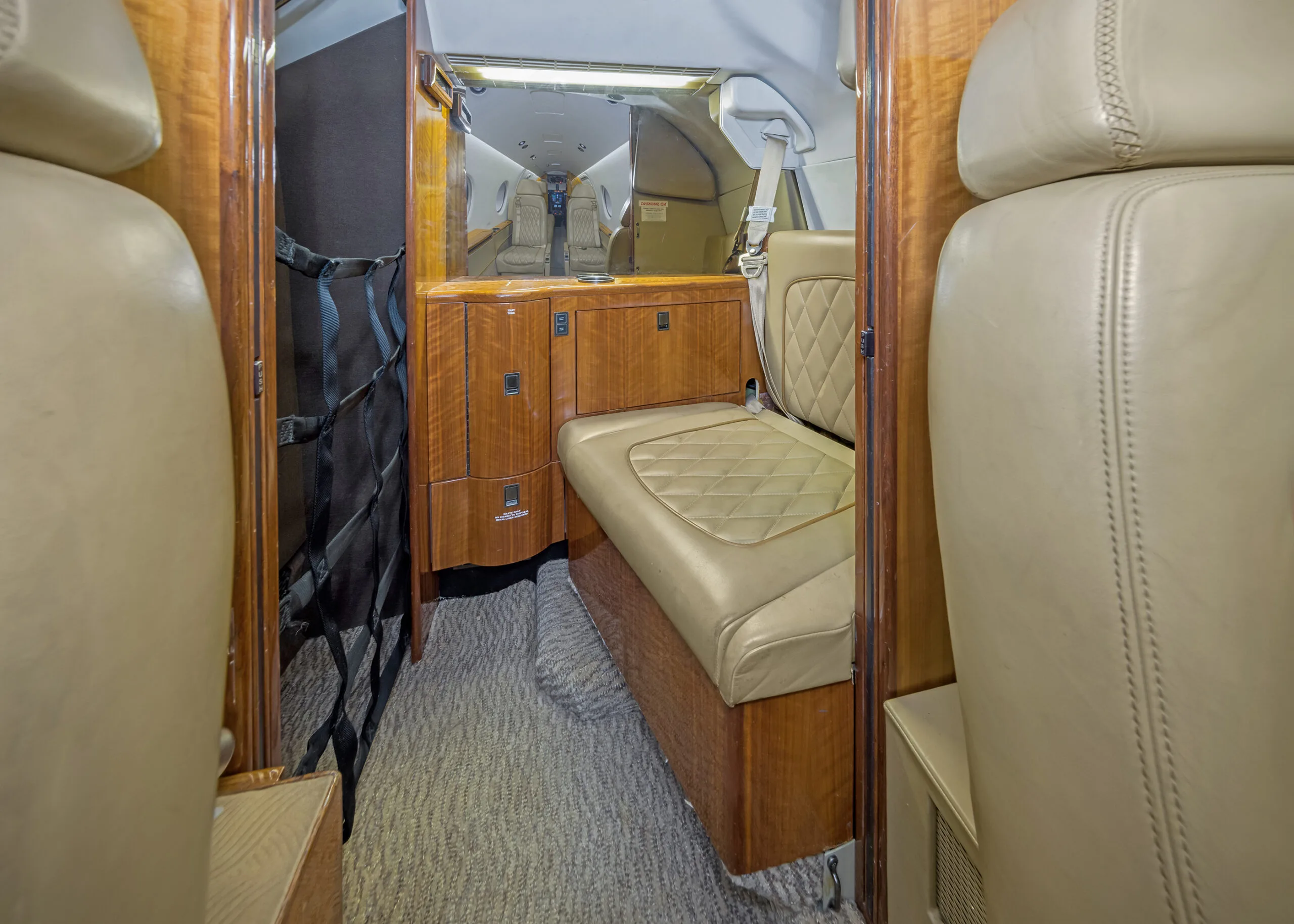 View of the aircraft interior with tan leather seats and wooden cabinetry.