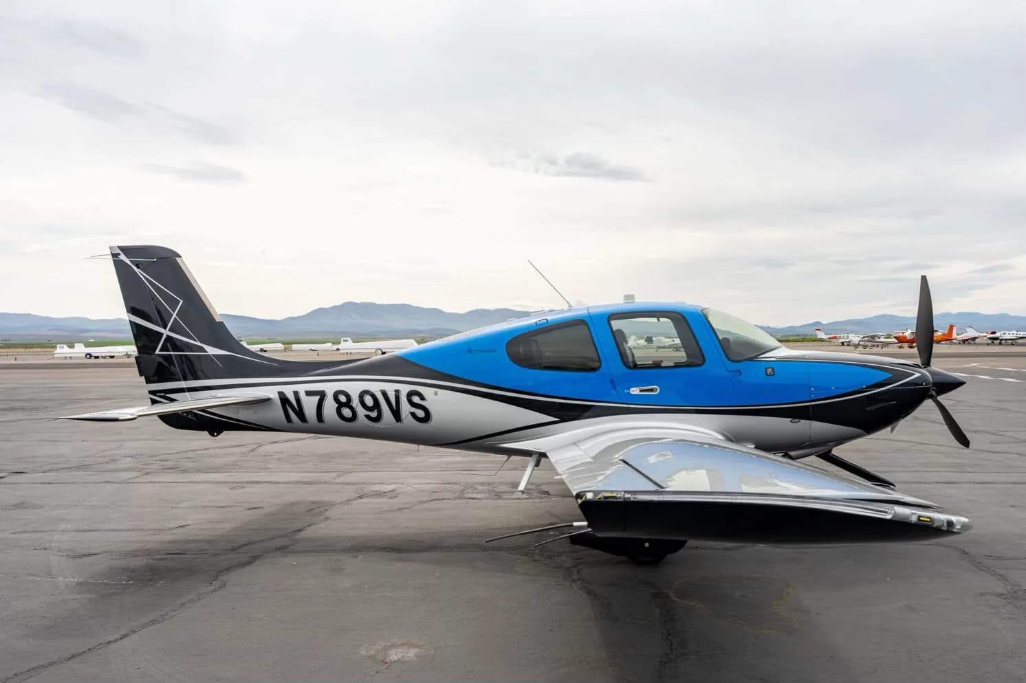 Side view of a black, blue, and silver single-engine aircraft with registration N789VS on an airfield, showing the wing.