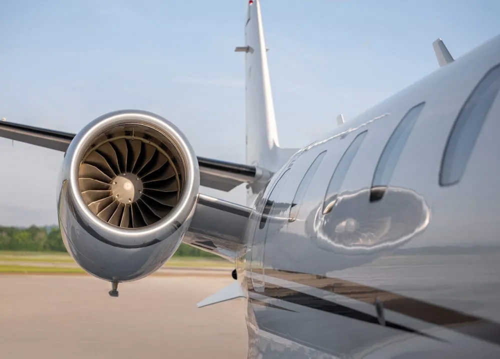 A close-up view of the jet engine and fuselage of a white business jet, showing the engine intake and passenger windows.