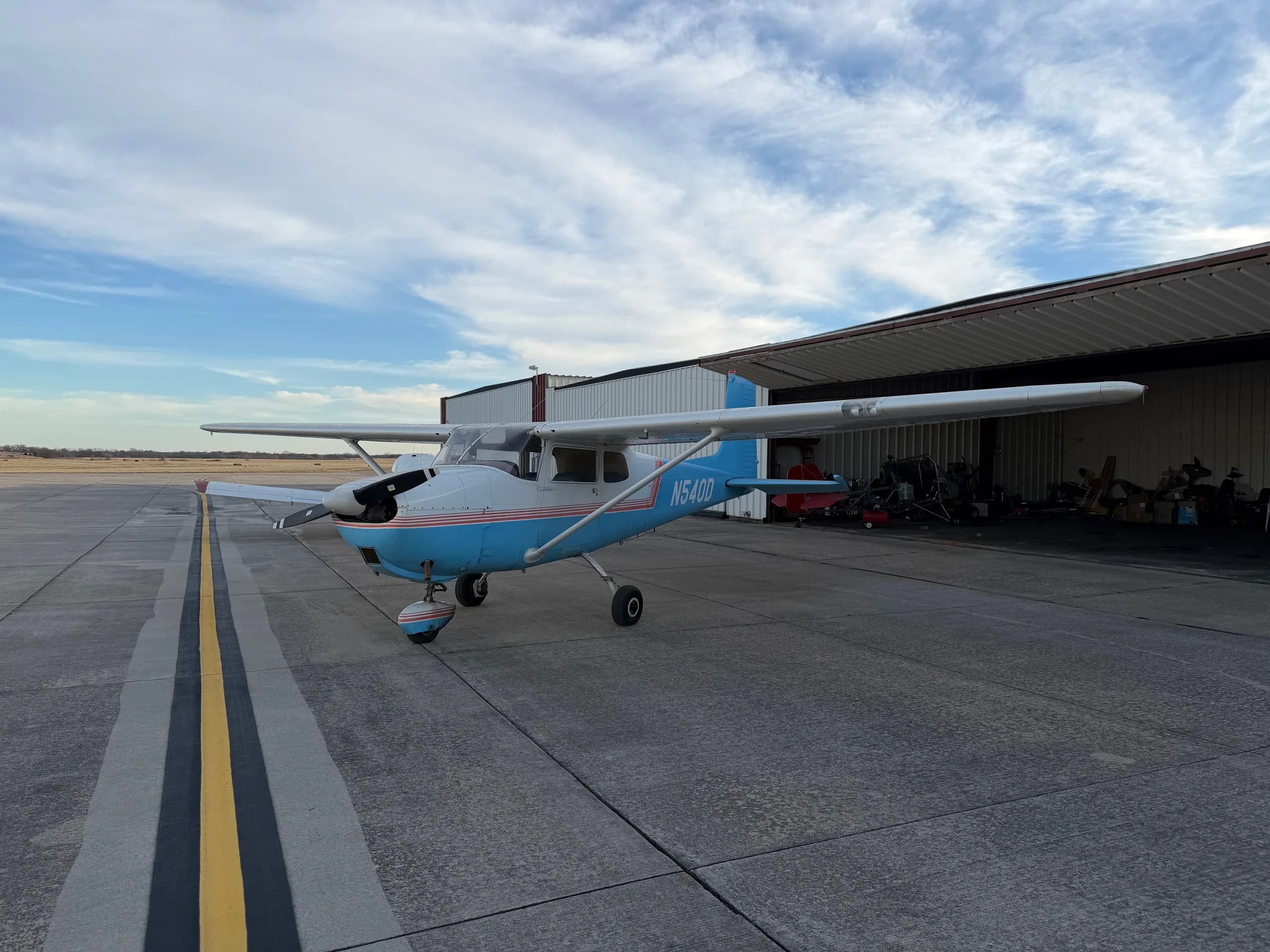 A slightly wider front-left view of a white and light blue Cessna 172, registration N540D, parked on an airfield.