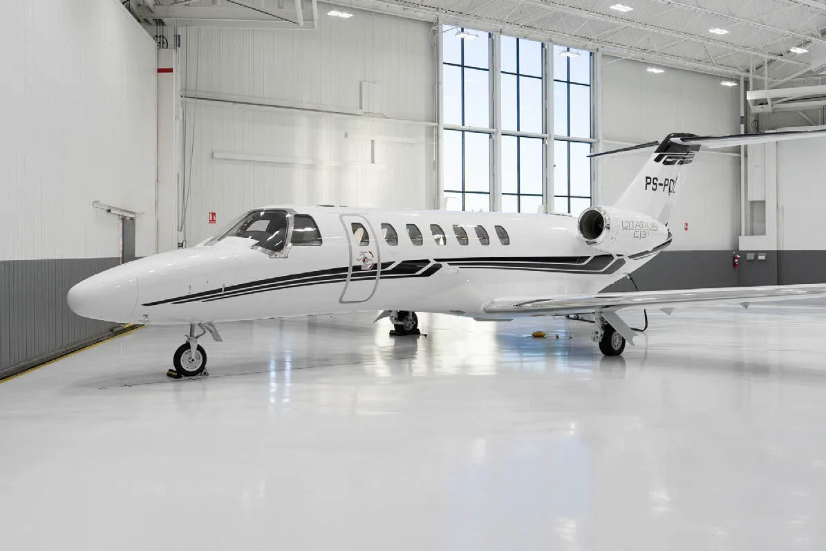 A full side view of a white Cessna Citation CJ3 private jet with black and grey stripes, parked in a clean hangar.