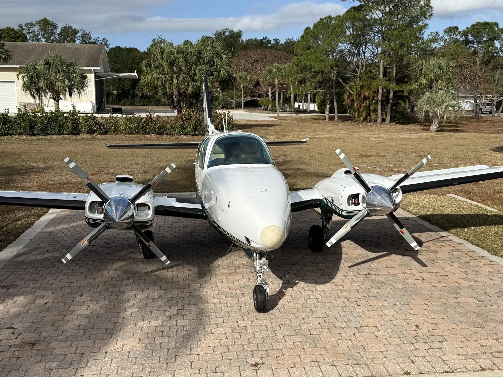 A head-on view of a white and green twin-engine Beechcraft Baron aircraft with tail number N288P parked on a brick driveway.