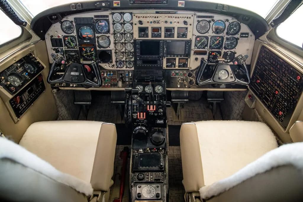 The cockpit of an aircraft with numerous analog gauges, screens, and controls, and two cream-colored seats.