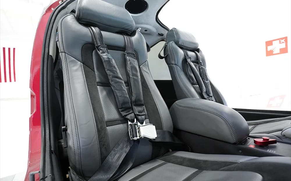 The gray and black leather front seats of a Cirrus SR22 aircraft, showing the seatbelts and armrest.