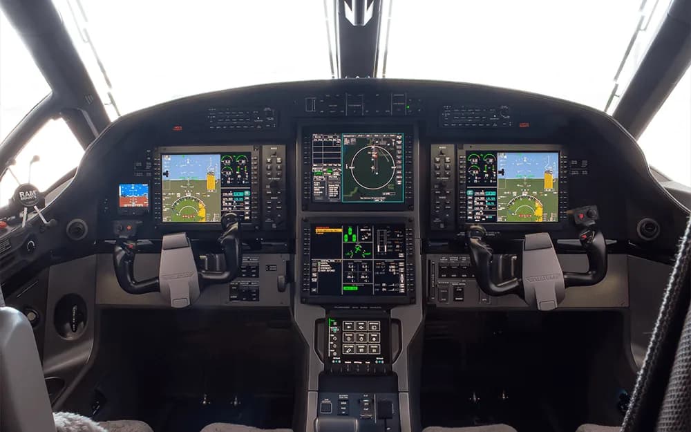 The modern glass cockpit of a Pilatus PC-12 aircraft with multiple large display screens and control yokes.