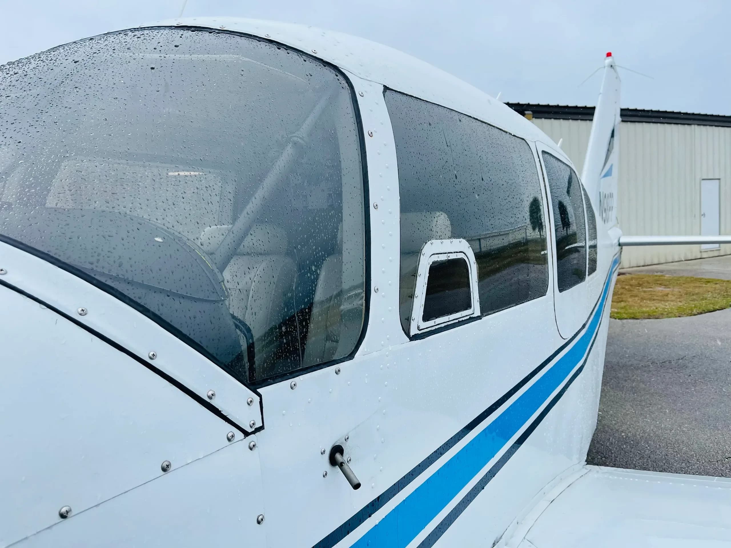 Close-up side view of the white aircraft's cockpit and cabin windows, showing raindrops on the surface.