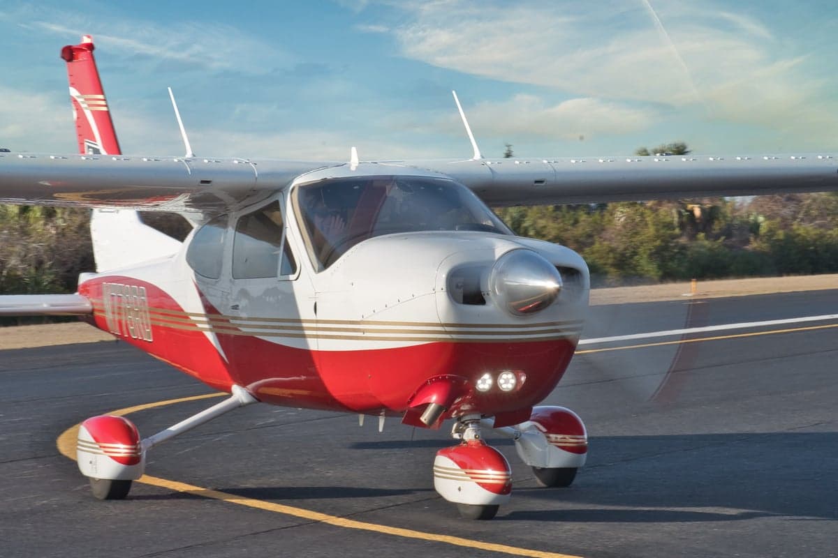 A low-angle front-side view of the red and white aircraft with gold stripes, taxiing on a runway.