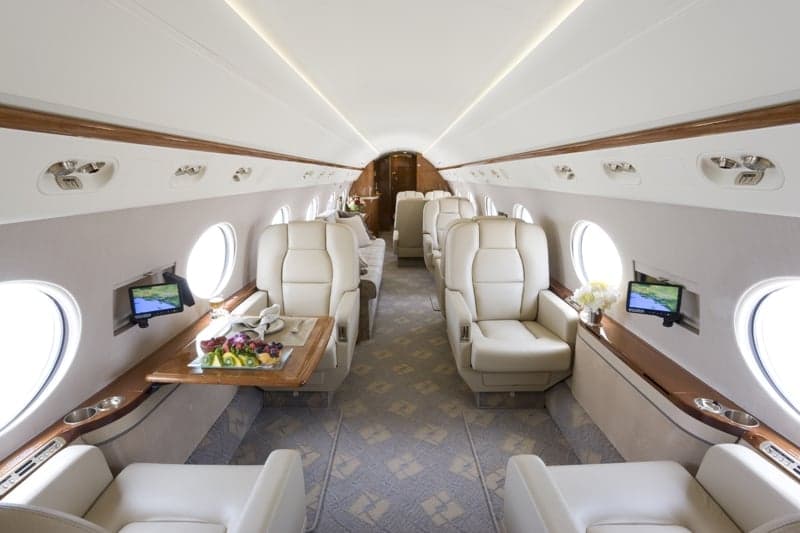 The interior of a private jet with cream-colored leather seats and wood trim.