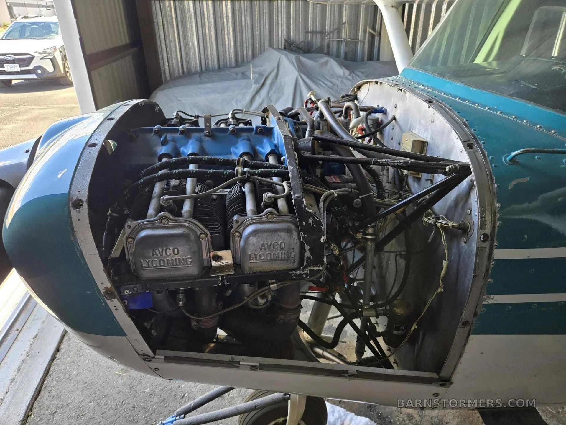 A close-up view of the exposed engine of a light aircraft, showing the cylinders and "AVCO LYCOMING" branding.